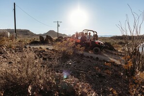 A rugged terrain with a vehicle and people, surrounded by dry vegetation and hills.