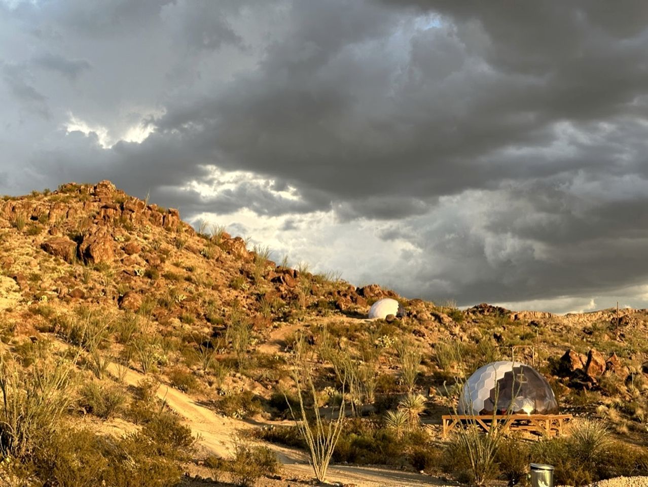 A desert landscape with rocky terrain and sparse vegetation, a spherical structure, and a dome-like building.
