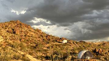 A desert landscape with rocky terrain and sparse vegetation, a spherical structure, and a dome-like building.