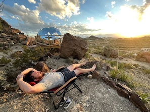 A person lying on a beach chair with a clear view of the ocean and a rocky landscape in the background.