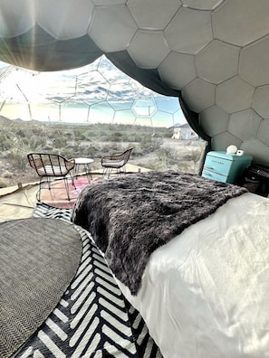 A room with a bed, two chairs, a small table, a heater, and a view of the landscape.