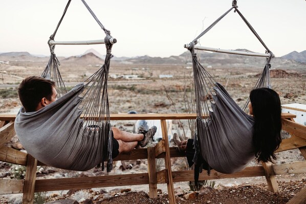 Two hammocks suspended from a wooden structure with a view of a desert landscape.