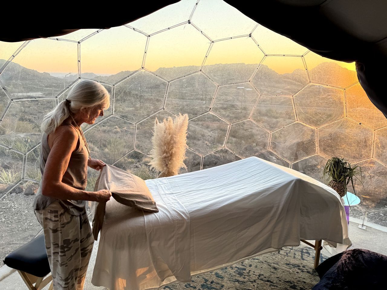 Une chambre avec un lit, une fenêtre ornée d’un motif hexagonal et une vue sur un paysage montagneux.