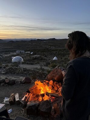 A desert landscape with a campfire, tents, and a person standing by the fire.