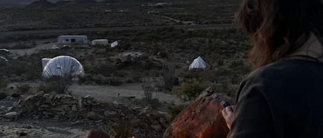 A desert landscape with a campfire, tents, and a person standing by the fire.