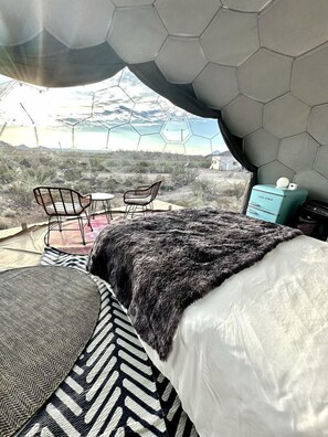 A room with a bed, two chairs, a small table, a heater, and a view of the landscape.