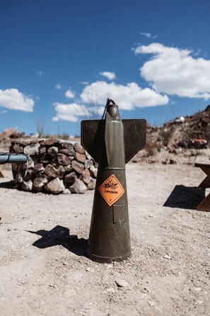 Ein bombenförmiges Objekt mit Warnhinweis vor blauem Himmel und einem Geröllhaufen.