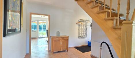 Une pièce spacieuse avec un escalier en bois, un radiateur et une porte donnant sur un espace extérieur.