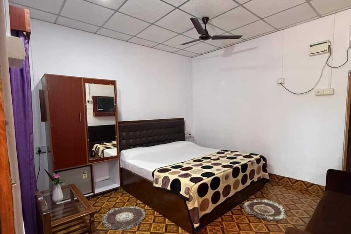 A bedroom with a bed, a desk, a chair, a wardrobe, a ceiling fan, and patterned flooring.