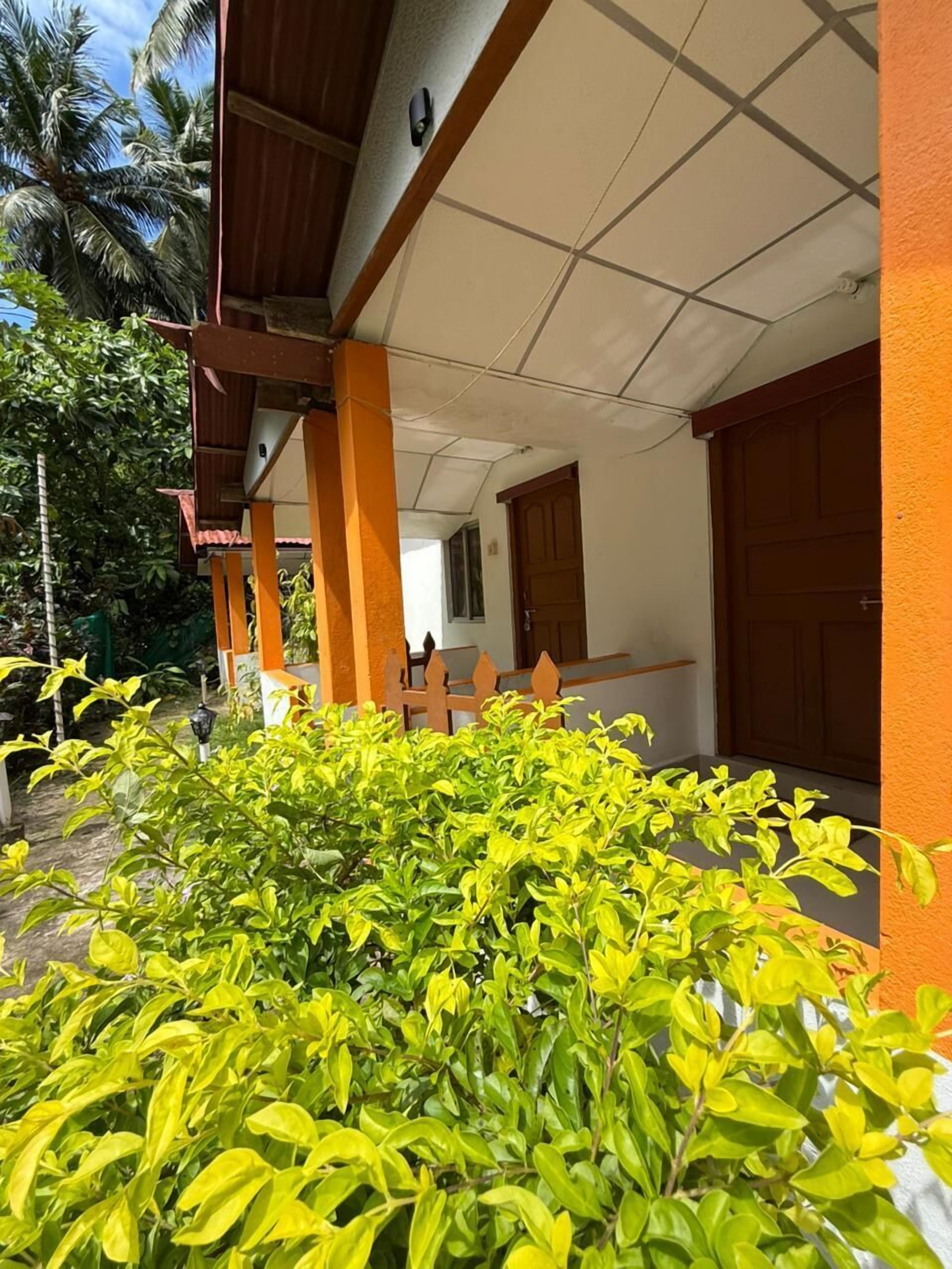 Un bâtiment doté d’un toit en tuiles et de piliers orange, entouré de verdure et muni d’une porte en bois.
