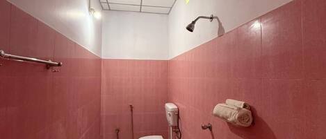 Un baño pequeño y cerrado con azulejos rosas, un inodoro, una ducha de mano, un perchero para toallas y un dispensador de agua verde.