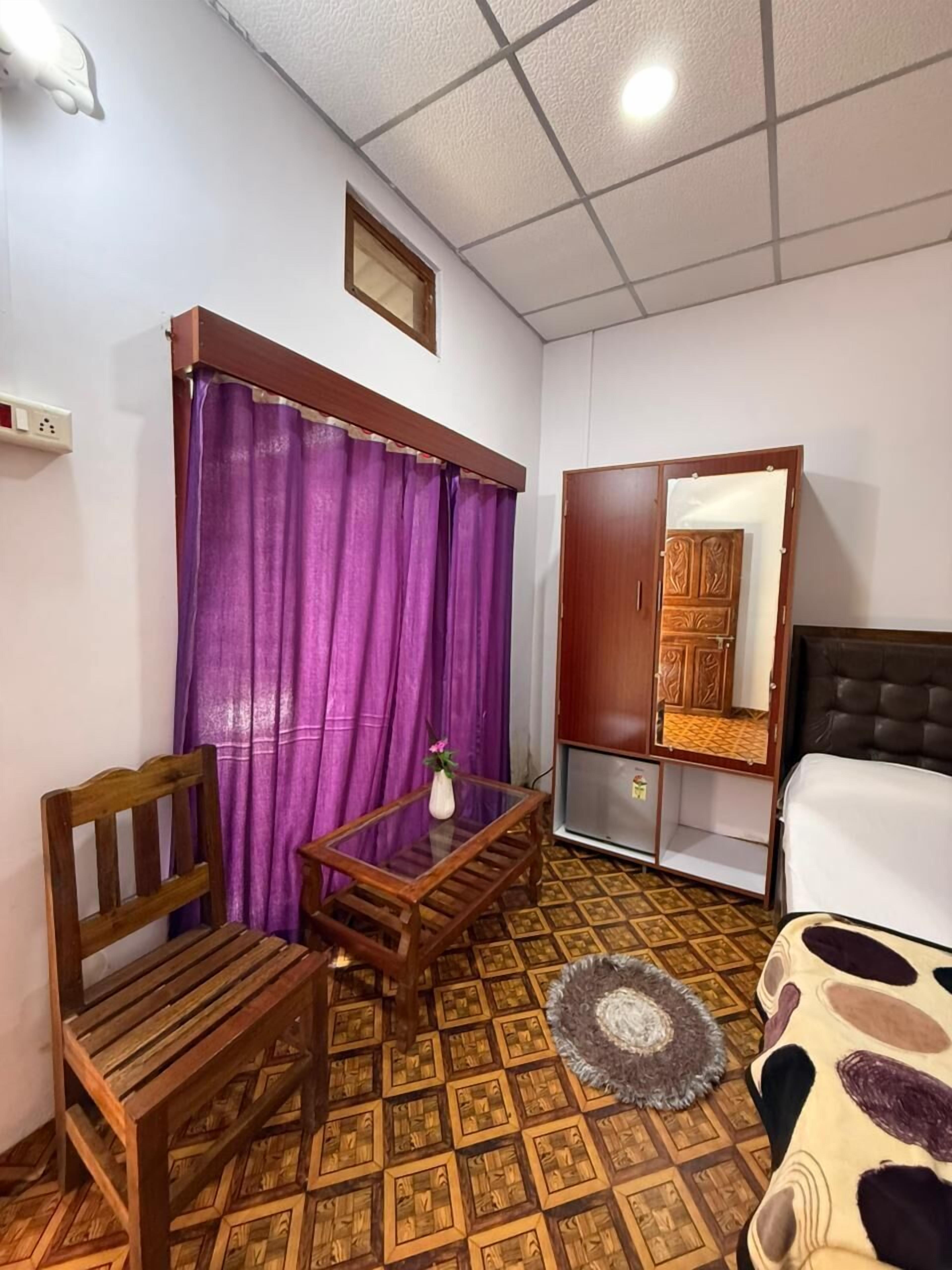 Una stanza con un letto, un armadio in legno, un tavolino con una sedia, tende viola e un pavimento decorato.