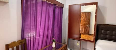 Una stanza con un letto, un armadio in legno, un tavolino con una sedia, tende viola e un pavimento decorato.