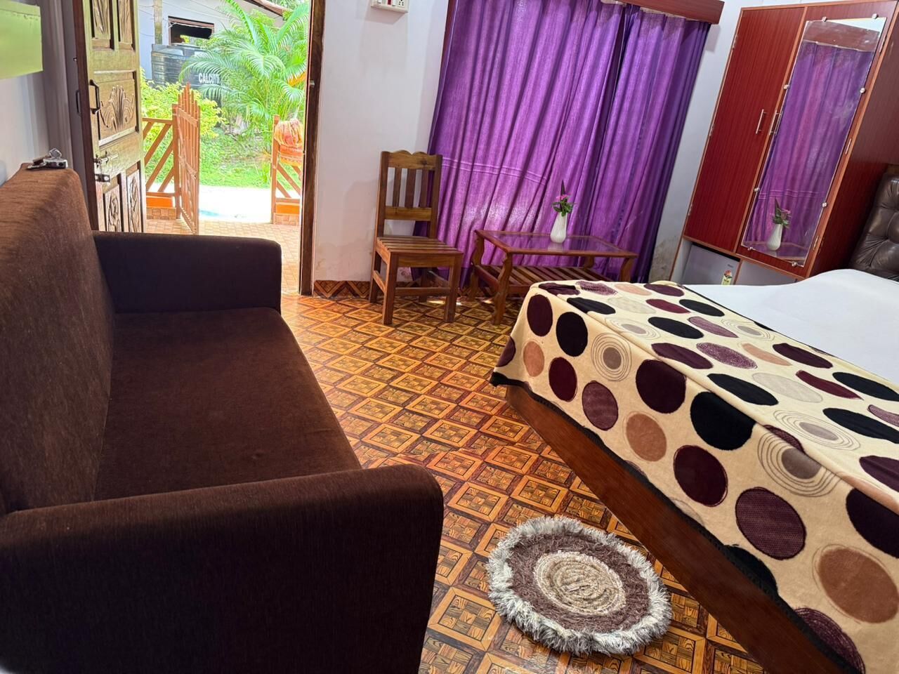 Ein Zimmer mit einer Couch, einem Bett mit Spitze, einem Sessel, einem kleinen Tisch und einem gemusterten Teppich.