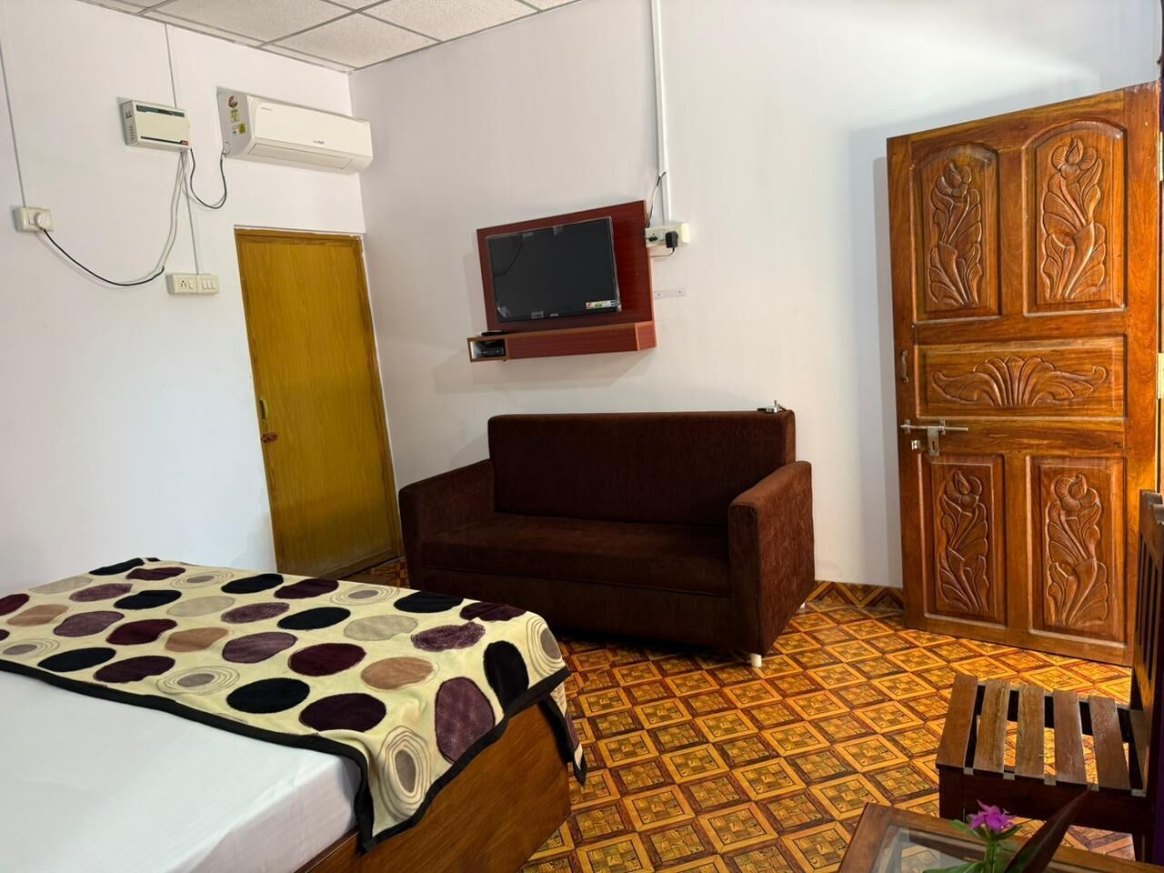 A hotel room with a bed, a sofa, a wooden wardrobe, and a small table with a vase.