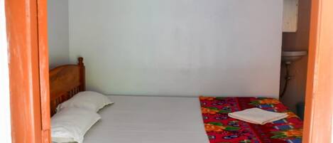 Una cama individual con cabecera de madera, un ventilador de techo y una mesita de noche con un libro.