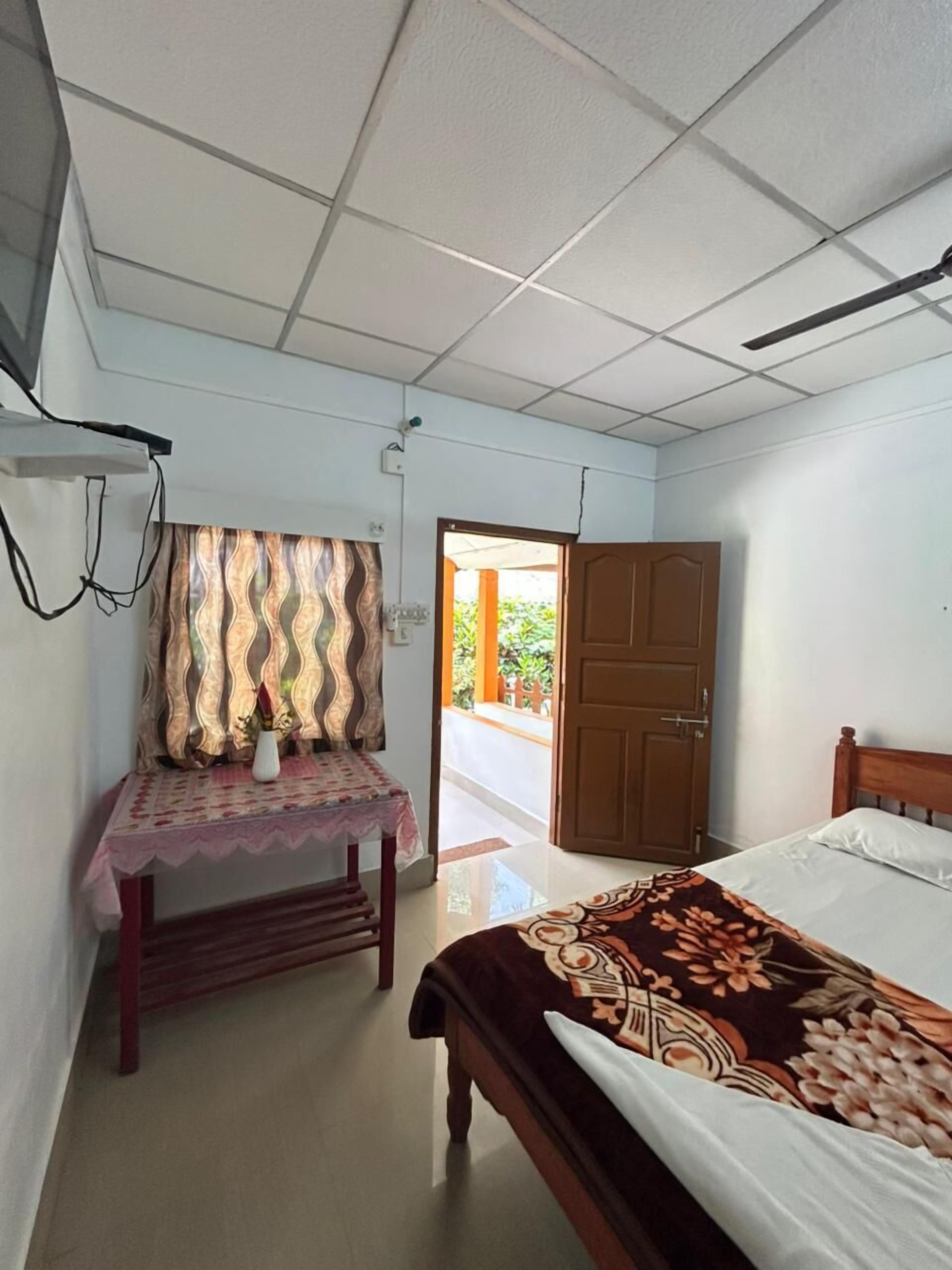 A bedroom with a bed, a desk, a chair, a ceiling fan, and a door leading outside.