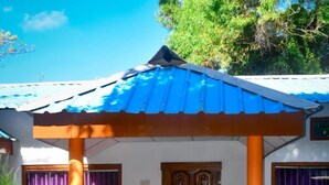 Una casa con techo azul, porche de madera y cortinas moradas.