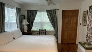 Ein Schlafzimmer mit einem Bett, einem Nachttisch, einem Sessel, einer Tür und einem Fenster mit Vorhängen.
