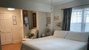 Une chambre à coucher avec un lit, une chaise, une table de chevet et une fenêtre avec des rideaux.