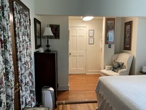 Un dormitorio con cama, una silla, un aparador, una lámpara y una puerta.