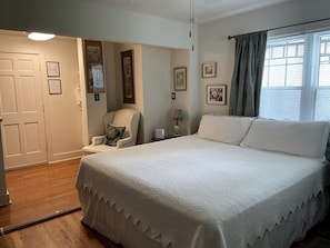 Un dormitorio con cama, una silla, una mesita de noche y una ventana con cortinas.