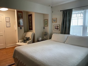 Un dormitorio con cama, una silla, una mesita de noche y una ventana con cortinas.