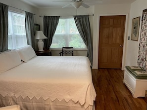 Un dormitorio con cama, mesita de noche, silla, puerta y ventana con cortinas.