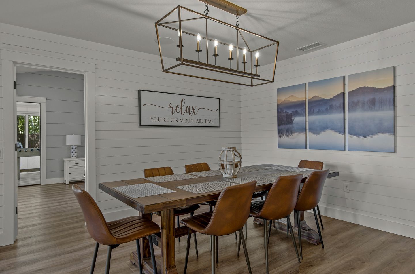A dining area with a wooden table, leather chairs, a chandelier, and a wall with a framed sign and paintings.