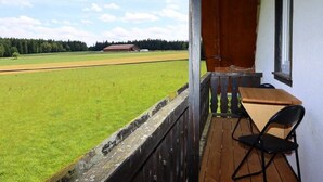 Een balkon met een tafel en stoelen, met uitzicht op een groen veld en een gebouw in de verte.