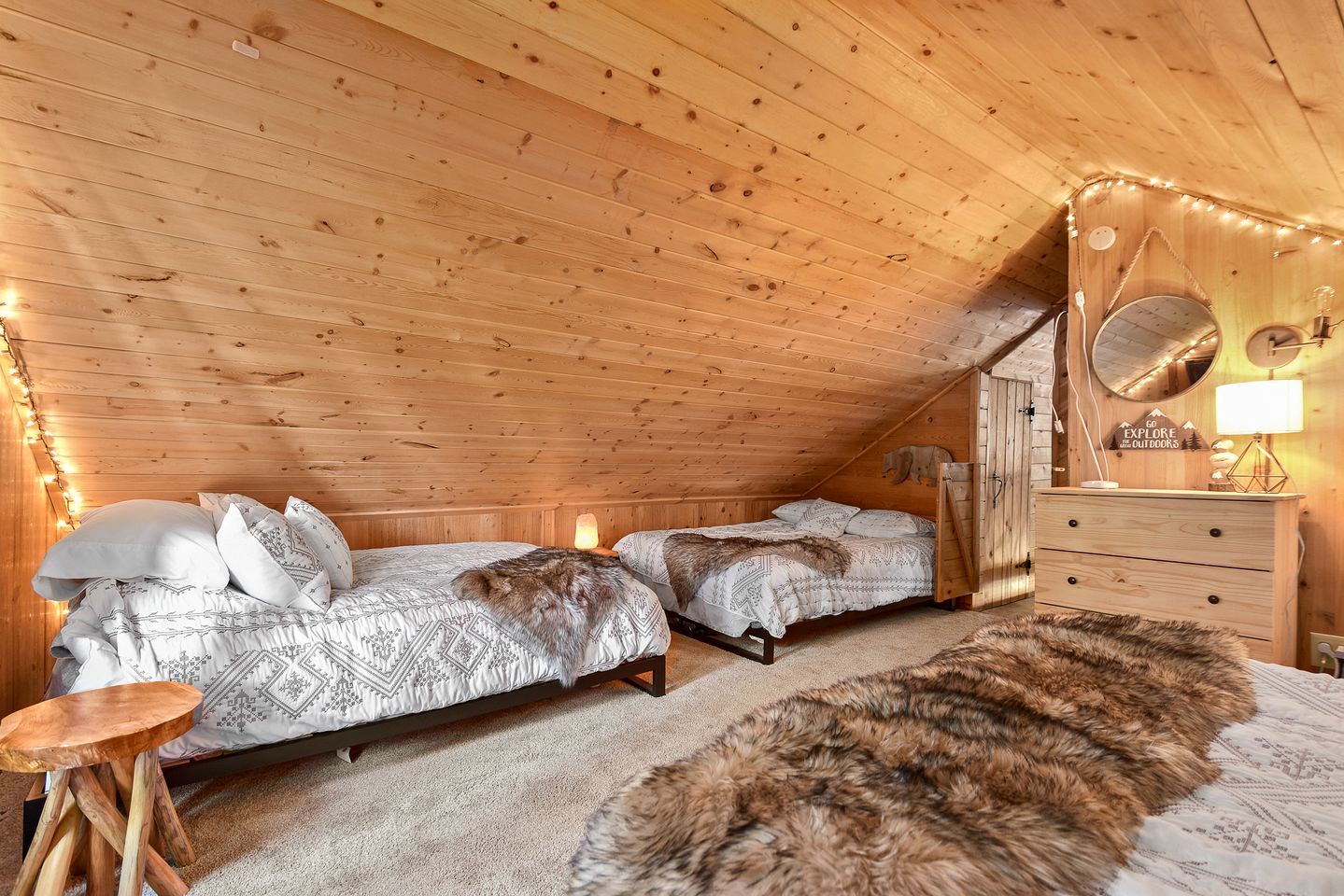 A cozy attic bedroom with two beds, a dresser, and a mirror.