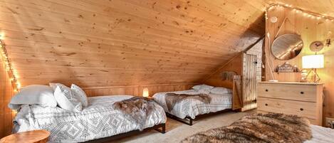 A cozy attic bedroom with two beds, a dresser, and a mirror.
