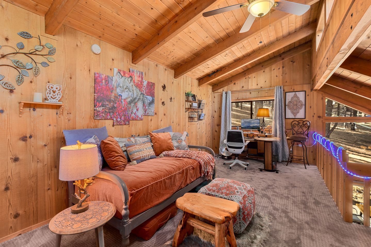 A cozy wooden cabin interior with a bed, desk, and computer setup.