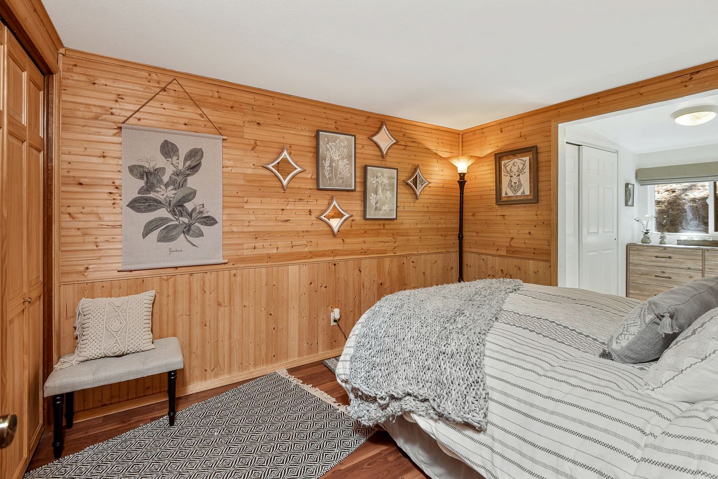 Ein Schlafzimmer mit Holzvertäfelung, einem Bett mit gemustertem Überwurf, einer Bank mit Kissen und Wandbildern.