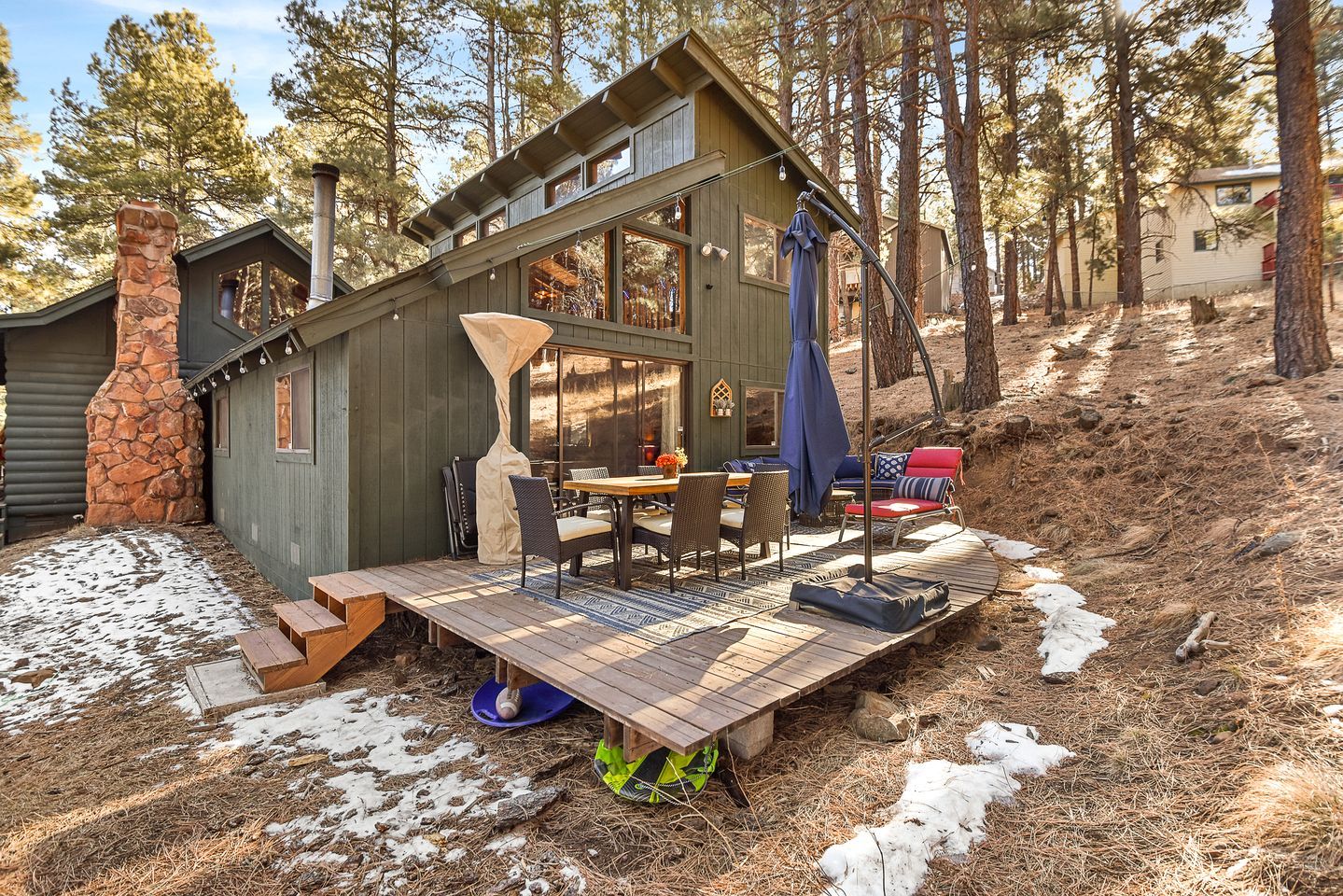 A cabin with a deck, outdoor seating, and a stone fireplace.