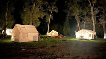 A campsite with several tents, each with a window and a door, surrounded by trees.