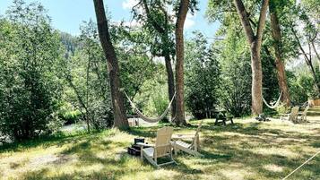 Un hamac, deux fauteuils Adirondack, une table de pique-nique et un petit abri de jardin, le tout situé dans un espace boisé.