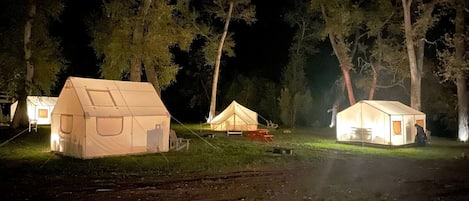 Un camping con varias tiendas de campaña, cada una con ventana y puerta, rodeado de árboles.