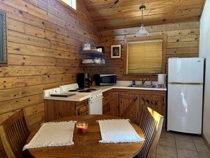 A wooden cabin interior with a kitchen area, a dining table with two placemats, a candle, and a refrigerator. - Cozy Cabin with Indoor Jacuzzi Great for Couples in Arkansas (Eureka Springs)