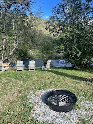 Un espacio al aire libre junto al lago con sillas Adirondack, una fogata y un río al fondo.