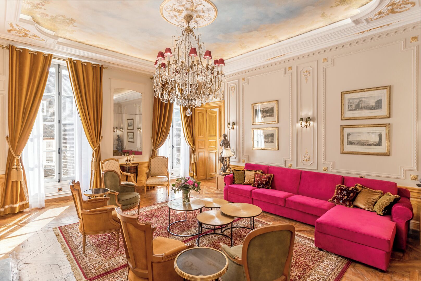 A luxurious living room with a chandelier, a pink sofa, and classic decor.