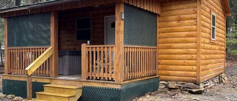 Une cabane en bois avec un porche, une table de pique-nique couverte et un sac à ordures.