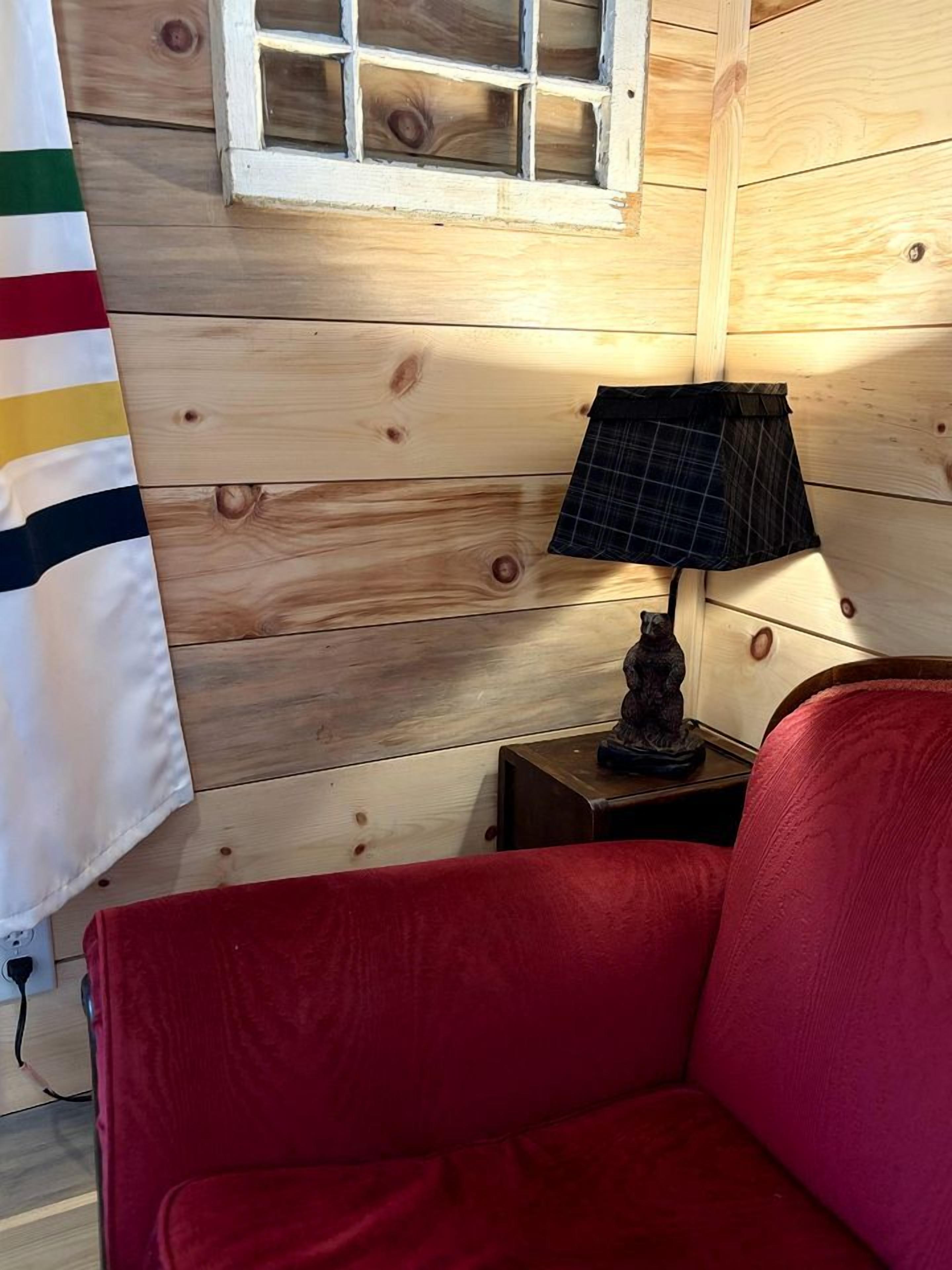 Une pièce chaleureuse avec un mur en bois, un canapé rouge, une lampe et une petite statue posée sur une table de chevet.