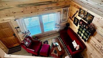 A wooden cabin interior with a red sofa, a small table, and a window with curtains.