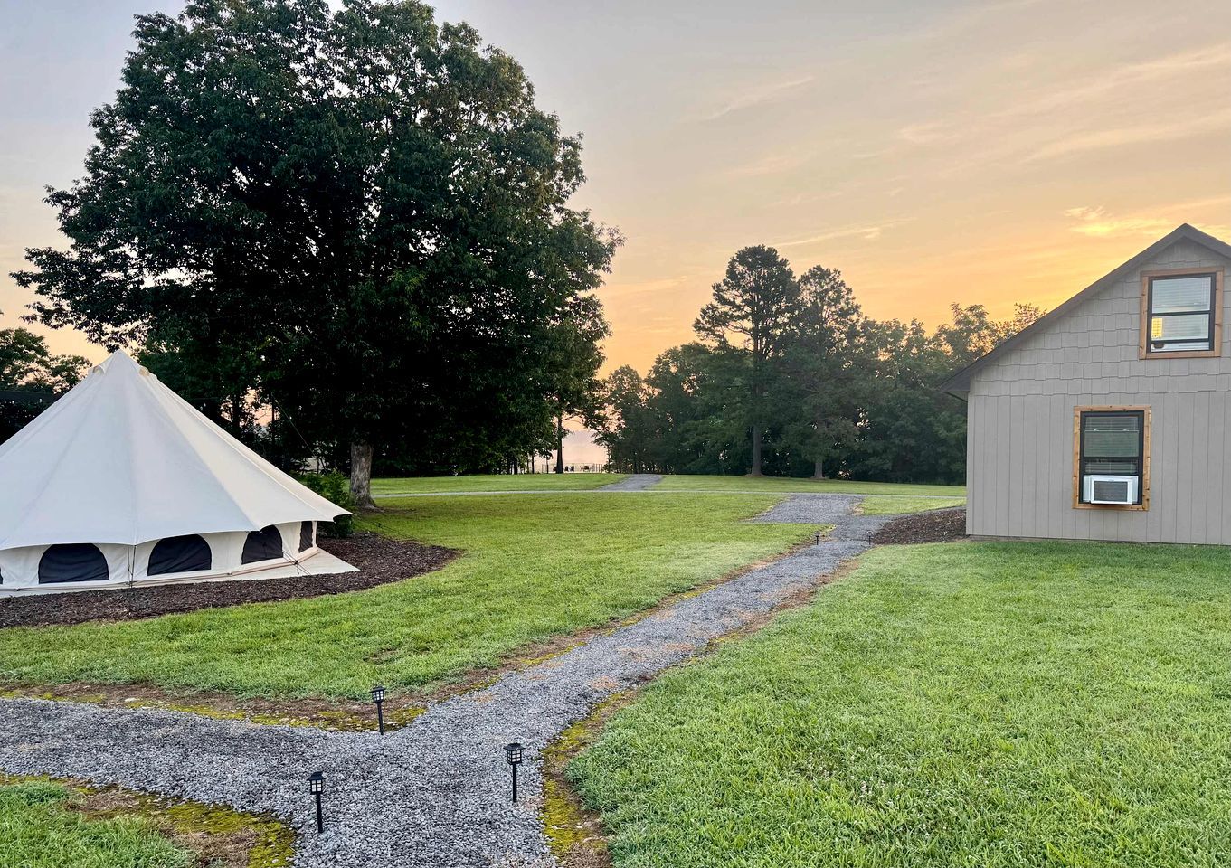 A grassy area with a white tent and a small building with a window.