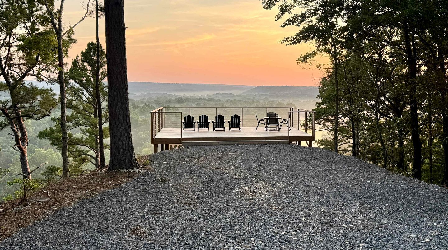 Un chemin de gravier mène à une terrasse en bois agrémentée de fauteuils Adirondack, d’où l’on peut admirer un paysage boisé.