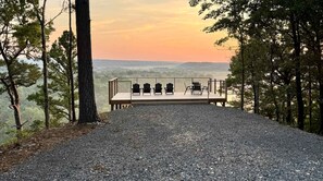 A gravel path leading to a wooden deck with Adirondack chairs, overlooking a forested landscape.