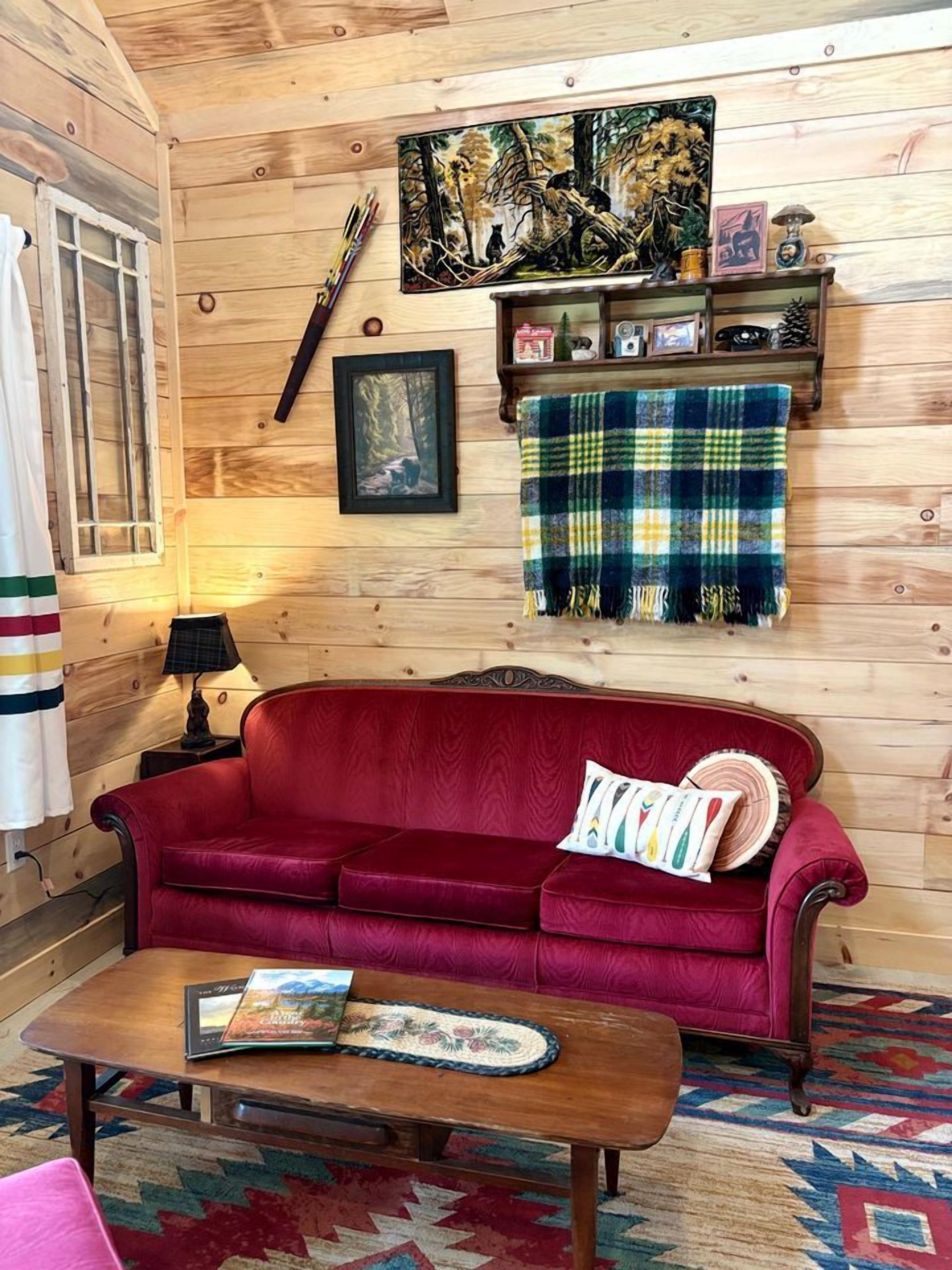 Une pièce chaleureuse avec un canapé rouge, une table basse en bois, une couverture à carreaux et un tableau encadré accroché au mur.