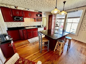 Een keuken met houten vloeren, rode kastjes, een centraal eiland en twee barkrukken.