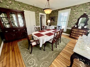 Un comedor con mesa de madera, sillas, una araña y pared cubierta de papel tapiz floral.